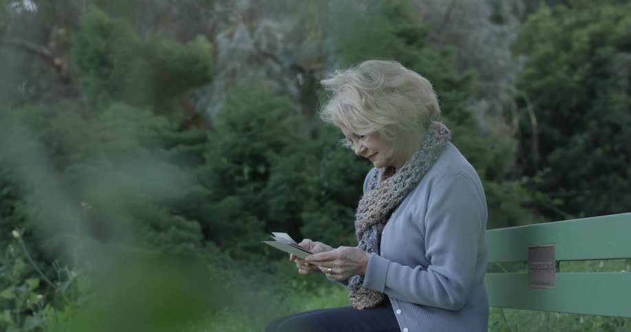 Woman looks at photographs while sitting on a park bench