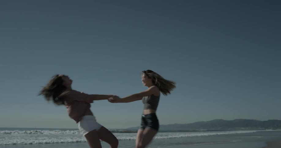 Two women hold hands and spin on the beach