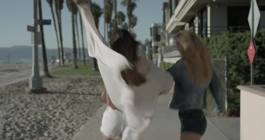 Two women frolic along sidewalk next to beach