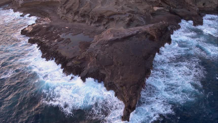 Foamy sea water clashes against the rocks of the shoreline on a sunny day