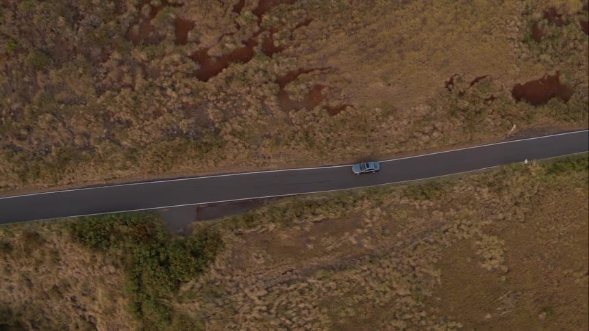 Car follows road through dry scrub lands