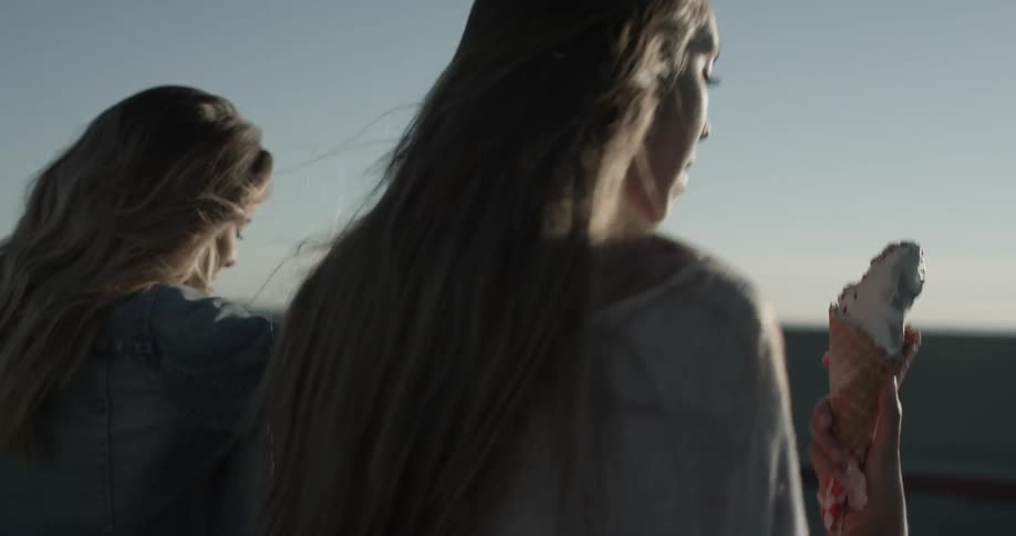 Two women walk across a parking lot with ice cream cones