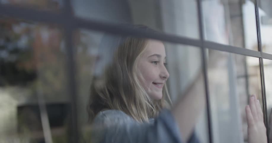 Two kids play a hand game on opposite sides of a window