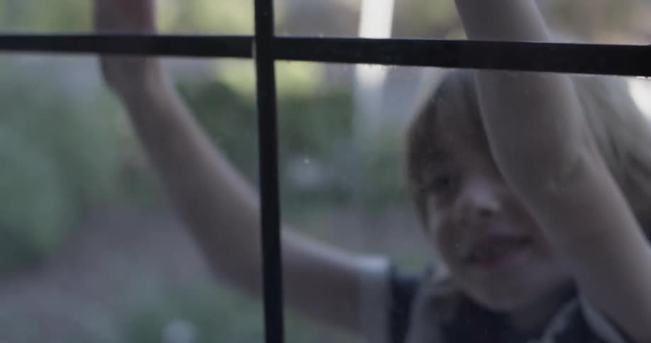 Outside a boy runs up to a window and presses his hands to it repeatedly
