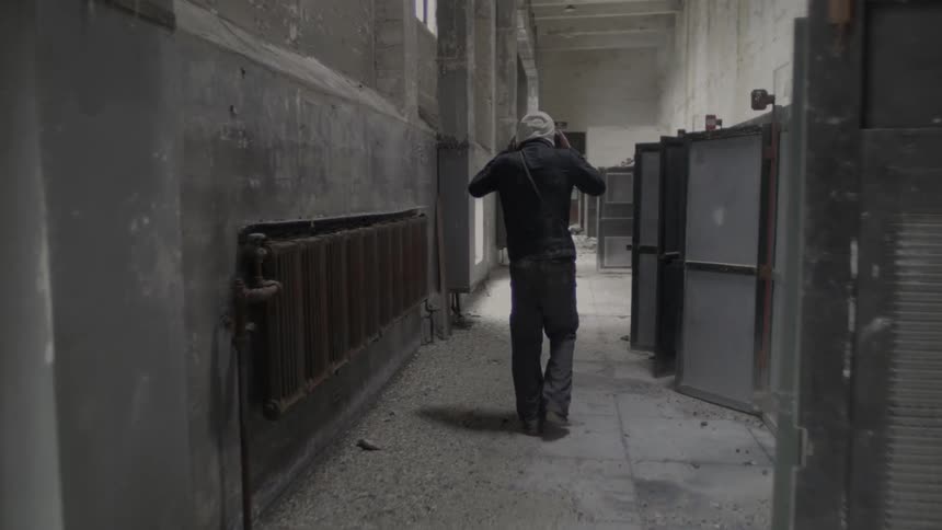 A man walks down a concrete hallway and removes his hoodie as he walks