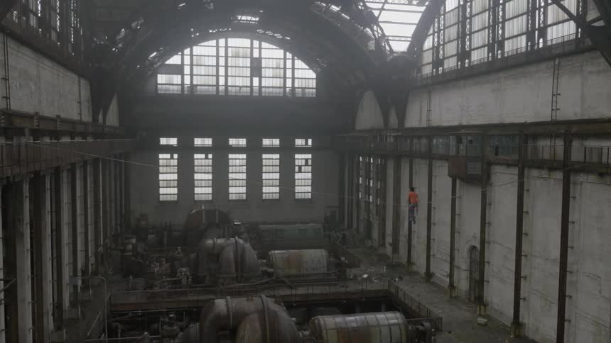 A man in an abandoned factory straddles a tightrope