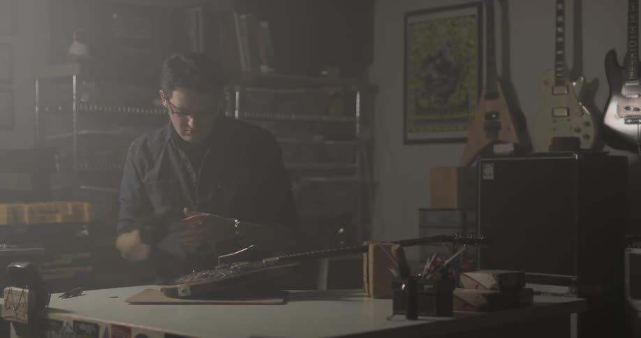 A man puts on gloves and begins to work on a guitar in a shop