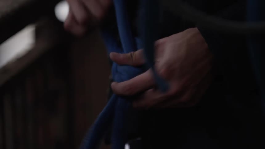Someone ties a special knot into a thick blue rope