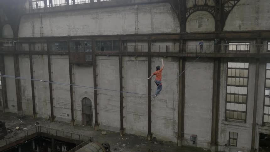 A person struggles to balance themselves on a high-wire in an old abandoned factory