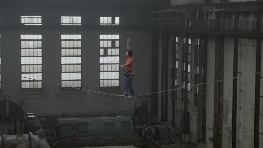 A person carefully balances on a tightrope in an abandoned building