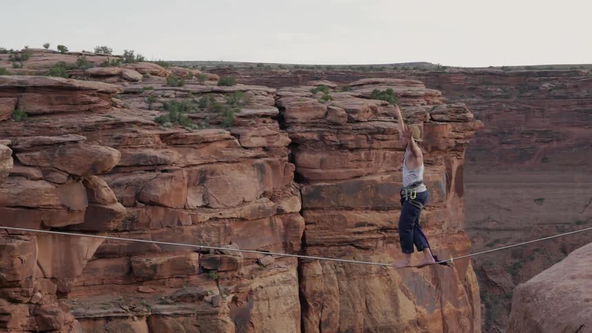 A man walks a tightrope between two canyon cliffs
