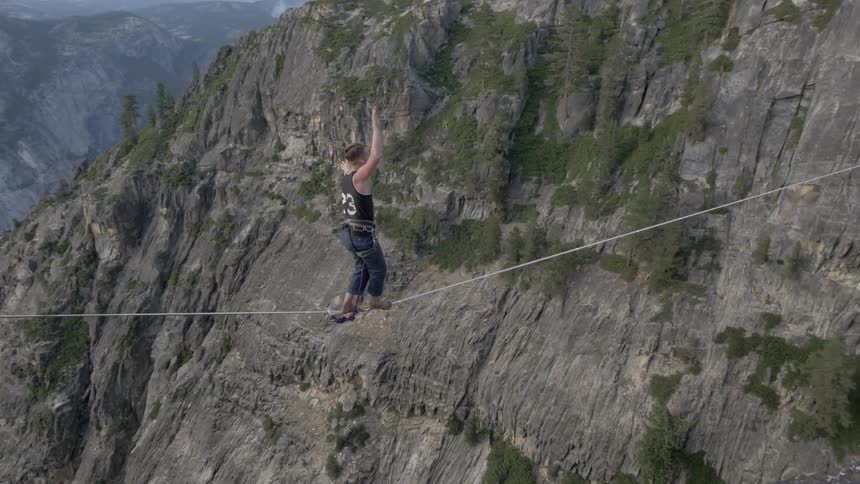 A man walks and balances on a tightrope suspended over a canyon
