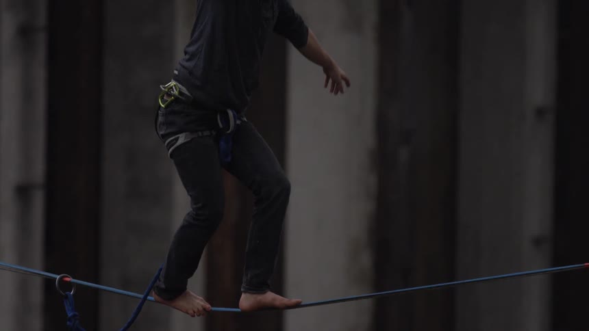 A man walks barefoot on a tightrope he is tethered to