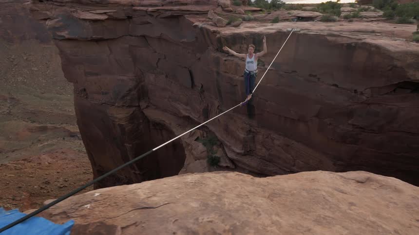 A man walking on a tightrope hung between two steep cliffs in the mountains