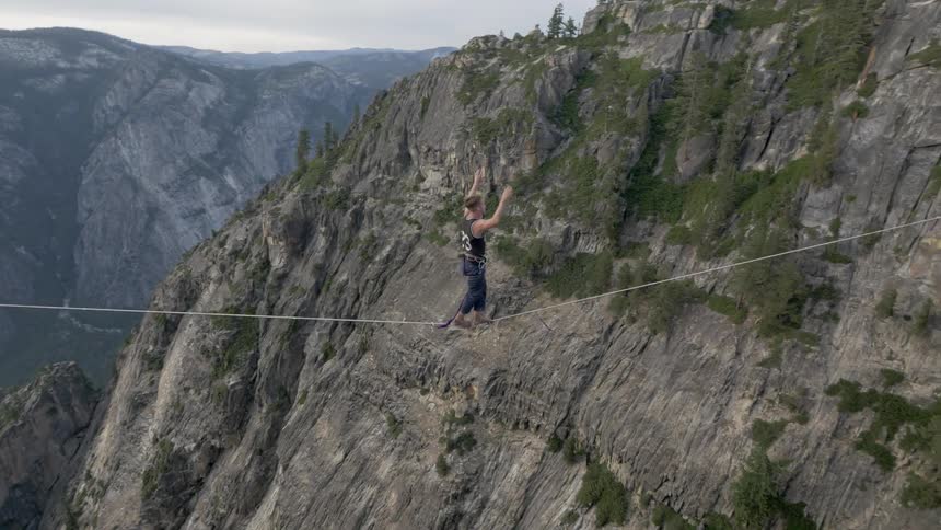 A man walking on a tightrope hung between two steep cliffs in the mountains