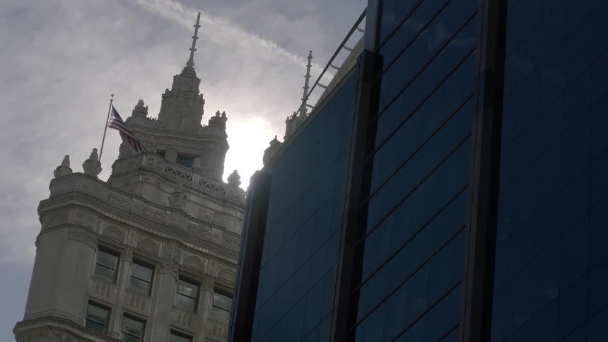A gothic building with a flag on top stands next to a modern building with dark windows
