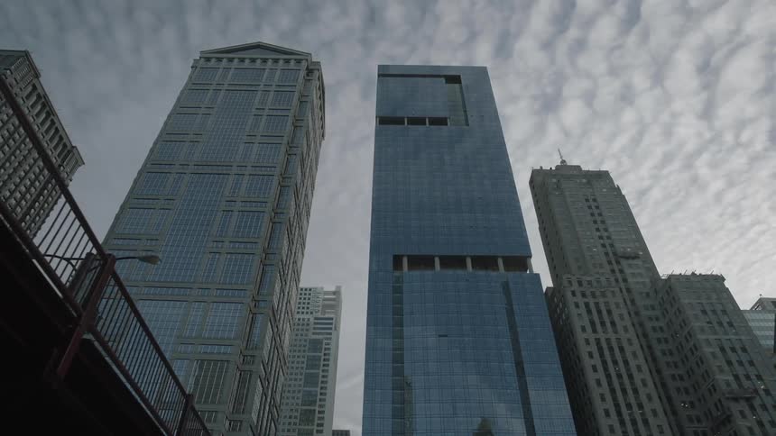 A view from the ground up while passing under a bridge and into an area where tall buildings are seen under a cloudy sky