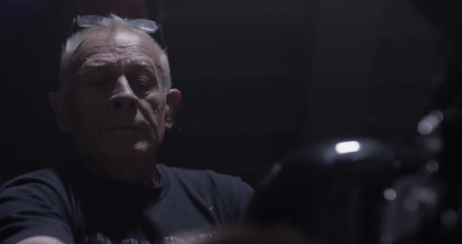 An elderly man sits on a motorcycle and turns the key
