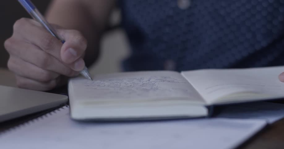 Person writes in notebook with pen