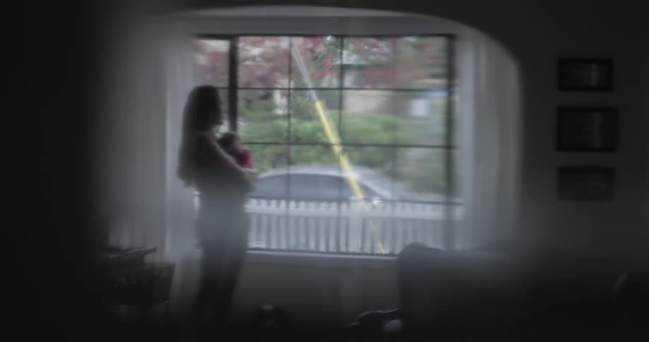 A woman holds a baby in front of a window