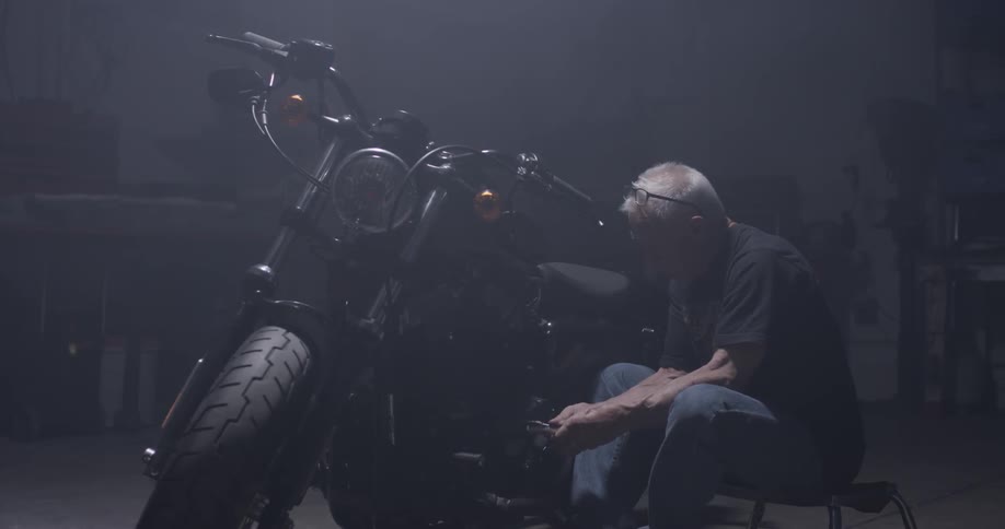 An old man uses a socket wrench to tighten a bolt on a motorcycle