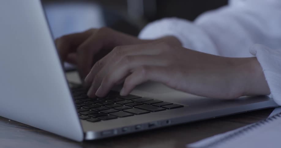 A person types on a silver laptop then writes in a notebook