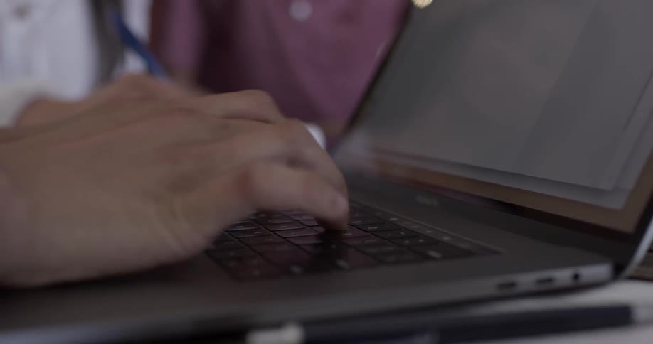 A person types on a laptop while two others sit next to them at the table