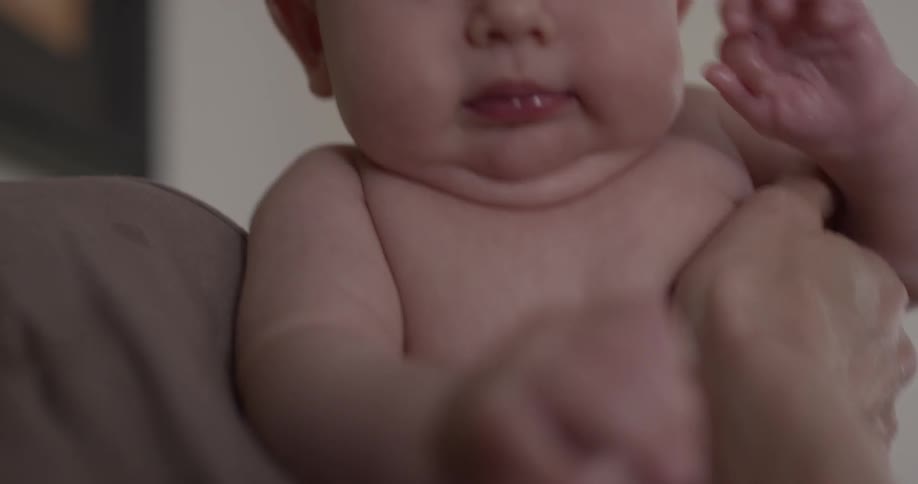 A mother's hands hold a baby and turn it towards the camera