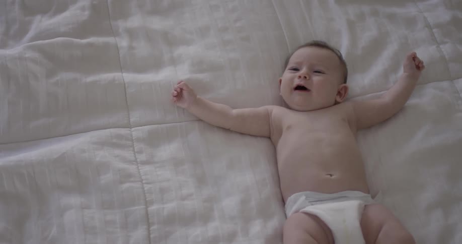 Baby lays on white bedspread and smiles