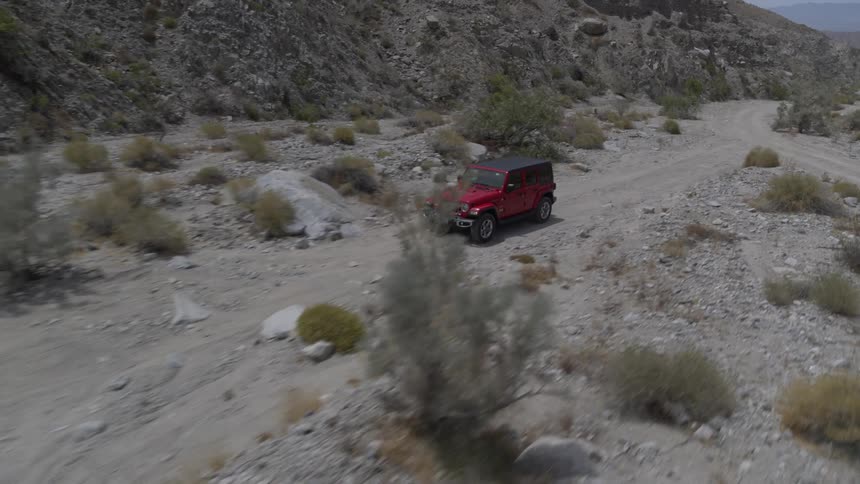 A red jeep drives down a dirt road in the desert