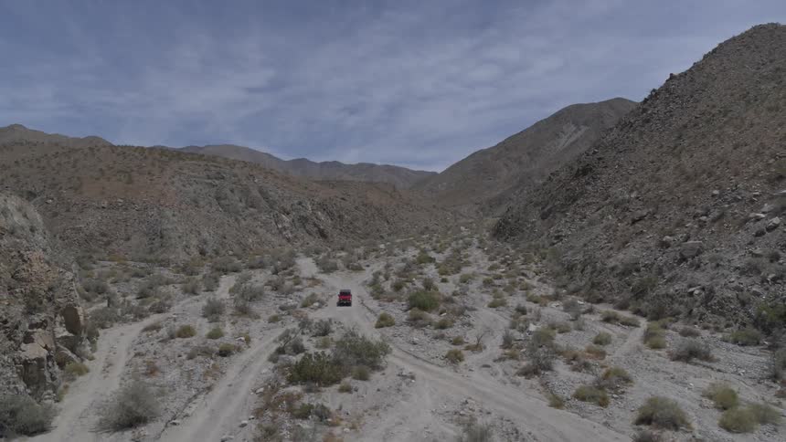 Red jeep car rides through the desert off roading on a blue sky sunny day
