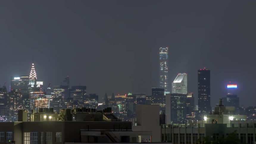 City is seen on a foggy night during a time lapse with bright skyline lights and people walking and lights flickering on and off