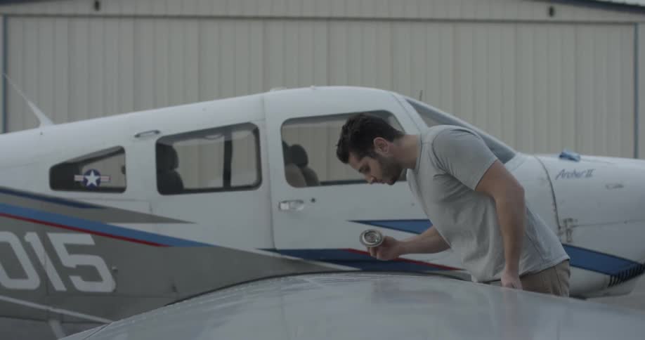 A man unscrews and then replaces a cap on the wing of an airplane