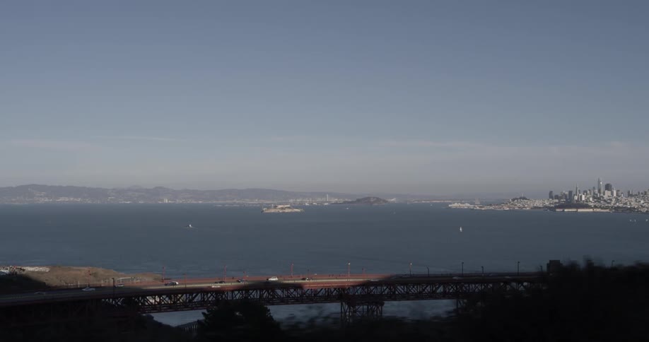 Boats out on the water behind a large bridge made of metal and a large city in the far background on a blue skies sunny day