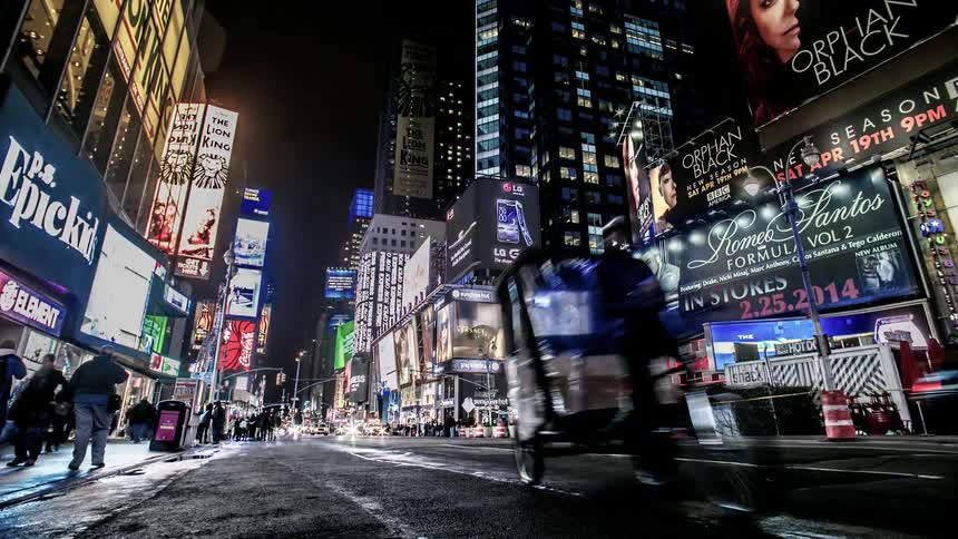 Colorful led signs illuminate a busy city road with streams of pedestrians and cars