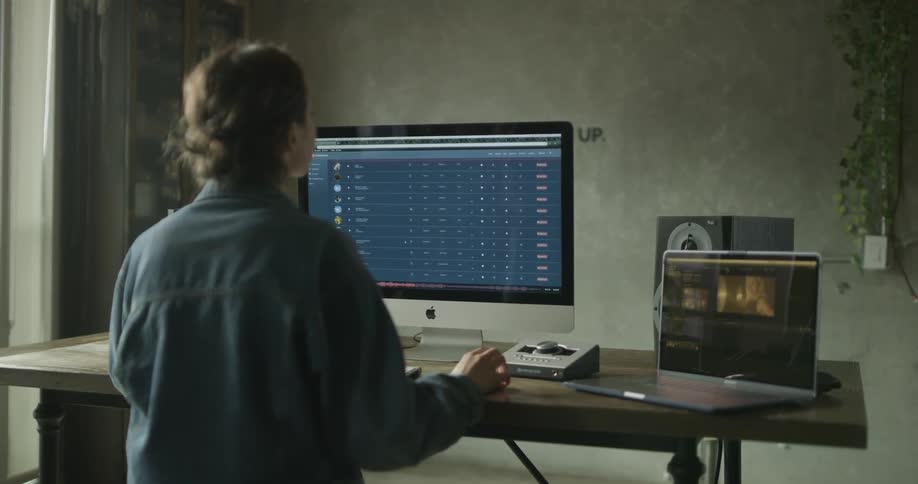 Woman sits at table with laptop and desktop and studies monitor