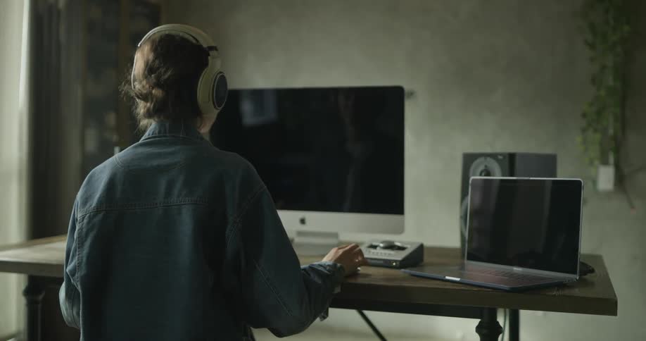 Woman wearing headphones works on computer and laptop