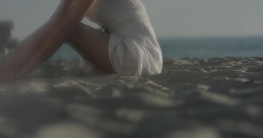 A woman sits on the sand running her hands through it