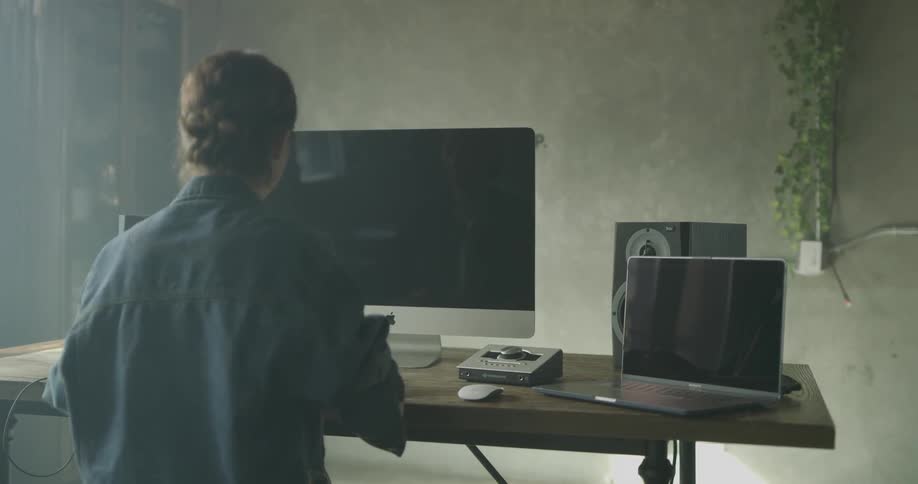 A woman is sitting and using her computer and laptop