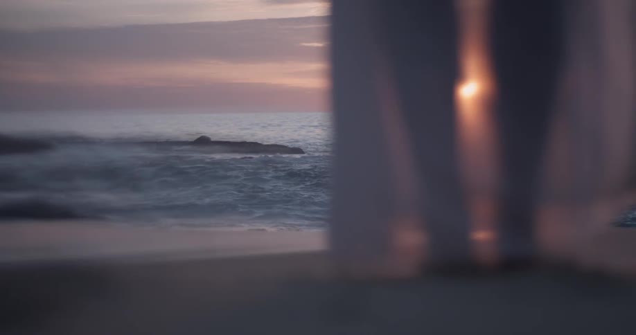 Person wearing translucent shawl looks out to where the ocean meets the sky