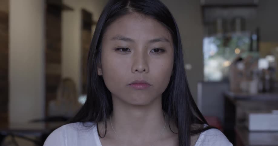 Woman sits in cafe making facial expressions