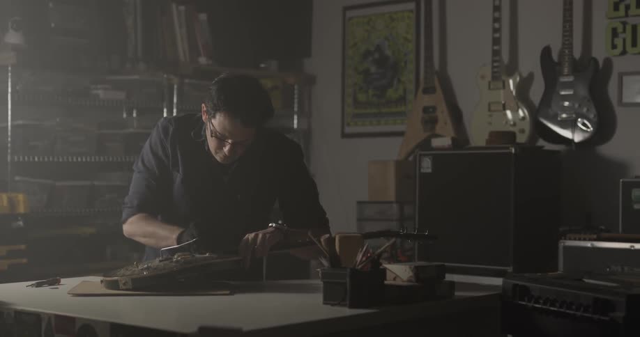 Man works on guitar bridge at a workbench