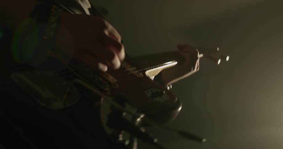 Man strums on his guitar and uses the whammy bar and jams in a dim lit room with a spotlight on him