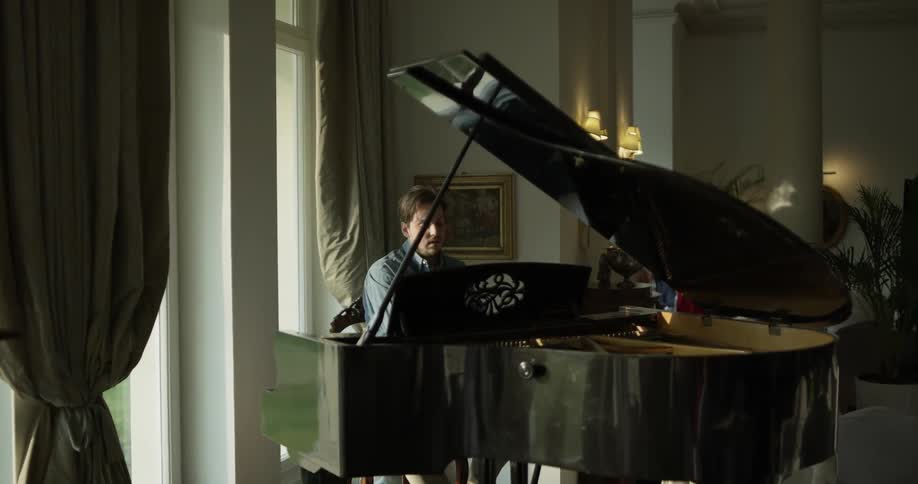 A man plays a piano in front of a window on a bright day