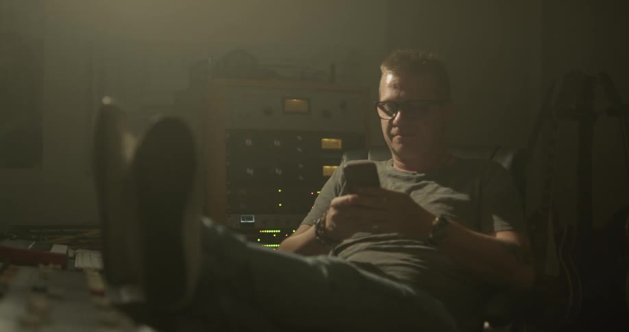 Man sits with heels on Audio mixer as he plays on phone