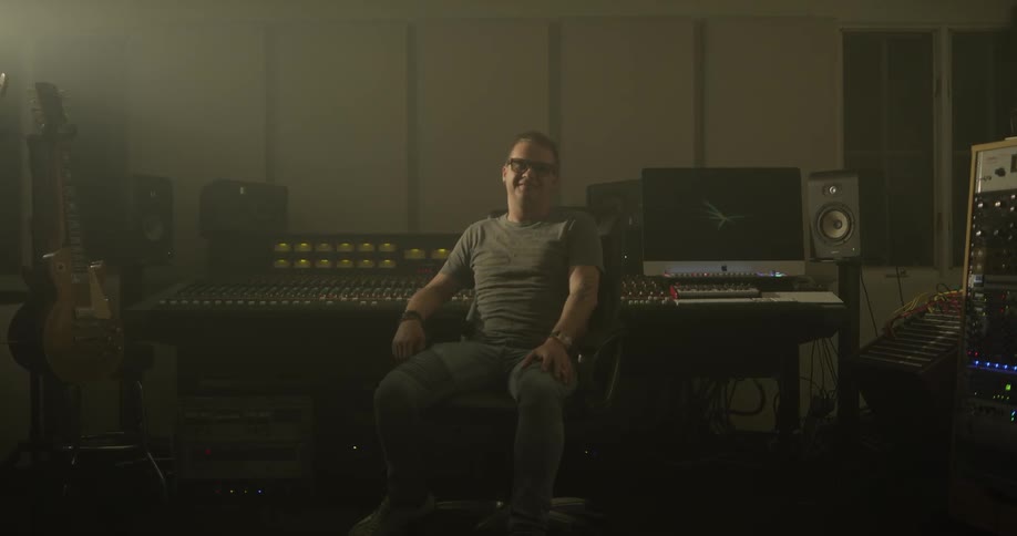 Man in chair in recording studio turns and gives thumbs up
