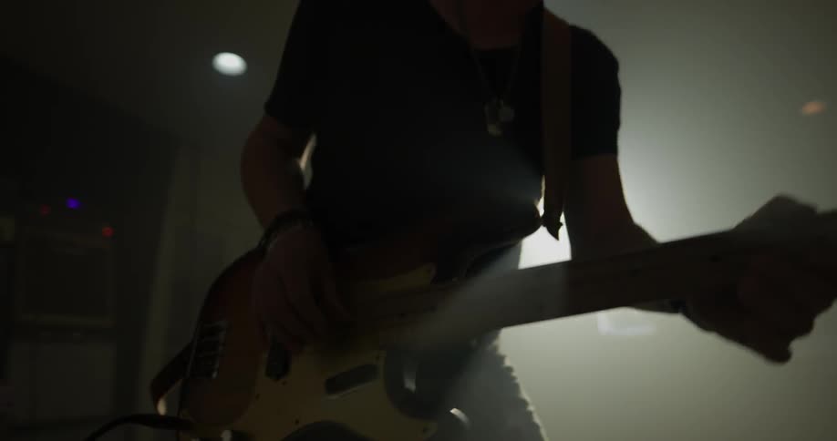 A young man plays an electric guitar in a dark room with one bright light