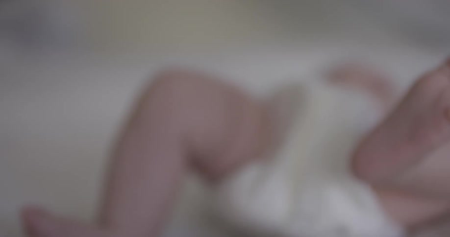 Baby kicks his feet around wearing a diaper laying down on a bed indoors