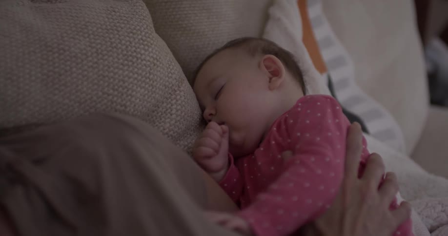 Person holds baby that sucks his thumb and sleeps