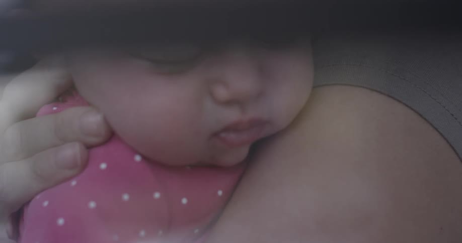 Someone folds a sleeping baby in a pink polka dot outfit
